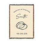 A beige custom woven blanket featuring a multicolored fringe on the sides and a black-and-white ringe on the top and bottom. The design includes the names [First Names] and [Last Name], rings, and the date [Date] in black text.