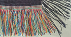 Close up of the edges of the woven blankets that are accented with vibrant, multicolored fringe along the two side edges and a contrasting classic black-and-white fringe along the top and bottom edges.