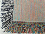 The back view of the woven blanket that is accented with a vibrant, multicolored fringe and a contrasting classic black-and-white fringe.