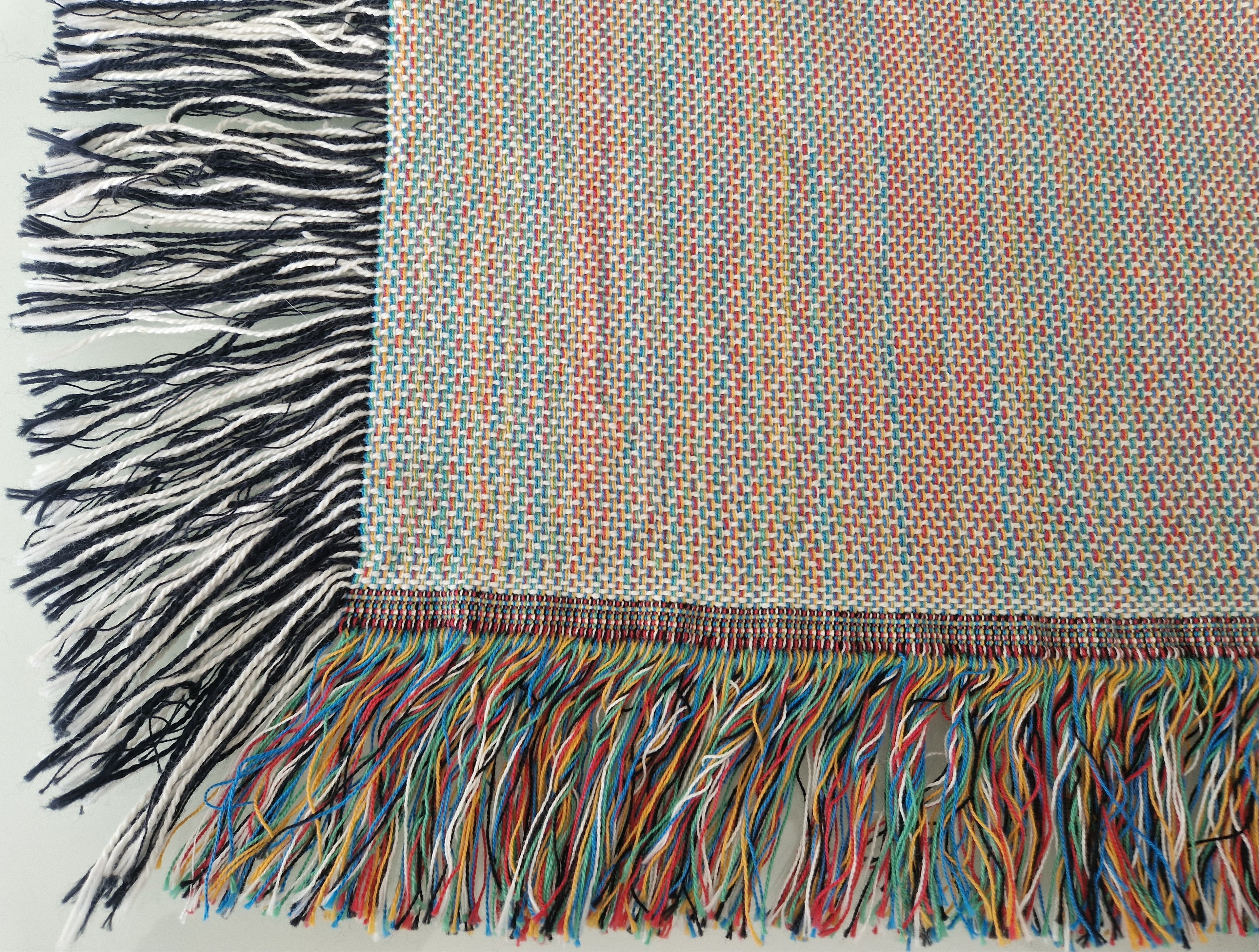 The back view of the woven blanket that is accented with a vibrant, multicolored fringe and a contrasting classic black-and-white fringe.