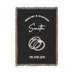 A black custom woven blanket that is accented with vibrant, multicolored fringe along the two side edges and a contrasting classic black-and-white fringe along the top and bottom edges. The design includes the names [First Names] and [Last Name], rings, and the date [Date] in beige text.