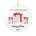 Round, white ceramic Christmas ornament. It features a vivid illustration of a stack of colorful wrapped presents, each secured with a ribbon. The names of family members are personalised and printed on a label in the front of each gift box. The main commemorative text, 'First Christmas as a Family of Three' and the year (e.g., 2025), is centered at the bottom of the ornament.