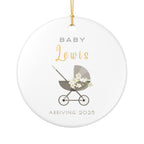 Round ceramic Christmas ornament featuring a baby carriage (pram) design accented with small flowers. Personalised text includes the baby's name, the year, and the phrases "Baby" and "Arriving." White background.