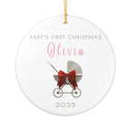 Round ceramic Christmas ornament featuring a baby carriage (pram) design accented with a red bow. Personalised text includes the baby's name, the year, and the phrase "Baby's First Christmas".  White background.