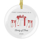 Round, glass Christmas ornament. It features a vivid illustration of a stack of colorful wrapped presents, each secured with a ribbon. The names of family members are personalised and printed on a label in the front of each gift box. The main commemorative text, 'First Christmas as a Family of Three' and the year (e.g., 2025), is centered at the bottom of the ornament.